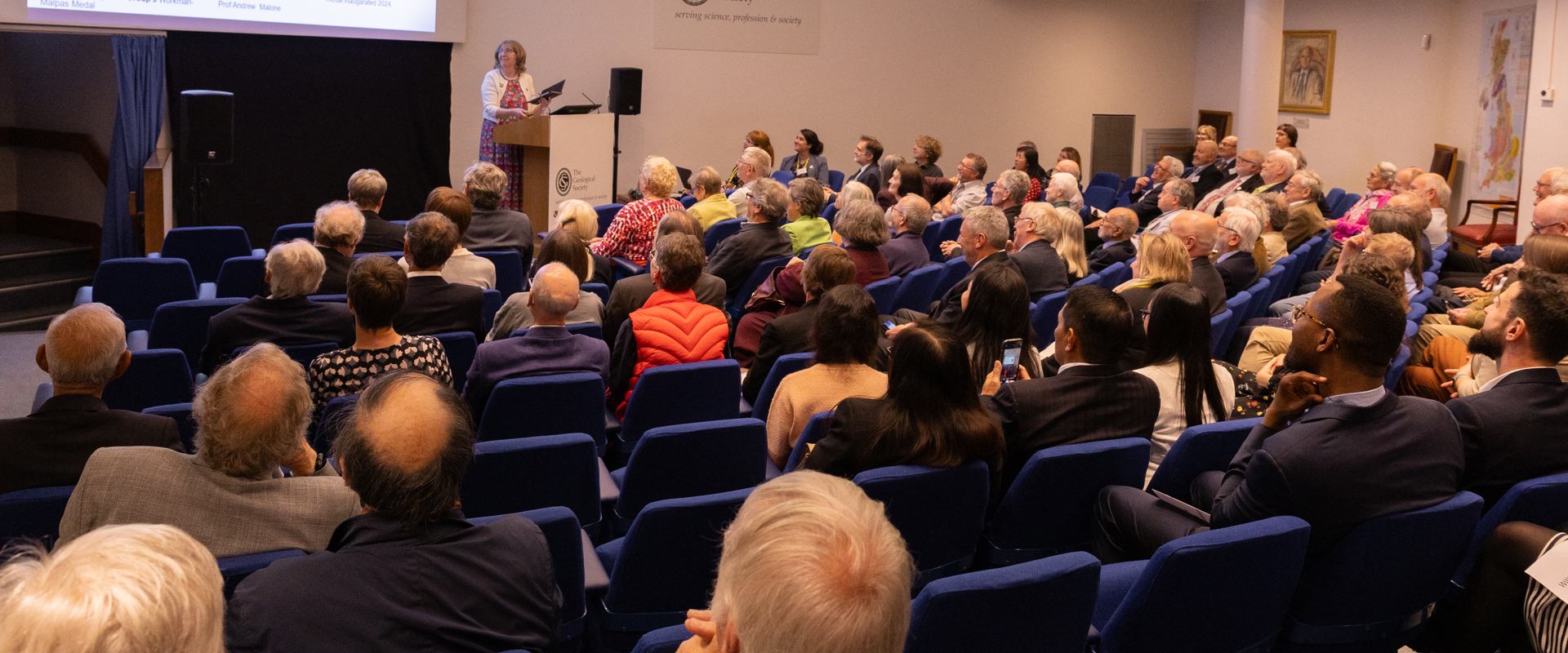 People seated in a lecture theatre listening to a woman speaking